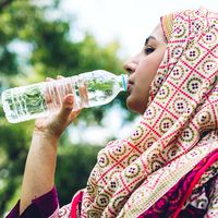 Woman wearing hijab drinking bottle of water outdoors