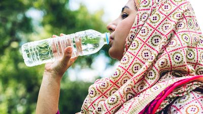 Woman wearing hijab drinking bottle of water outdoors