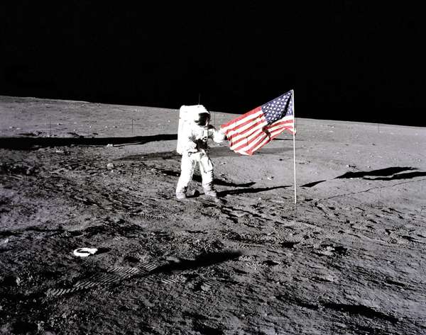 Apollo 12 astronaut Charles "Pete" Conrad stands beside the U.S. flag after is was unfurled on the lunar surface during the first extravehicular activity (EVA-1) Nov. 19, 1969. Footprints made by the crew can be seen in the photograph.