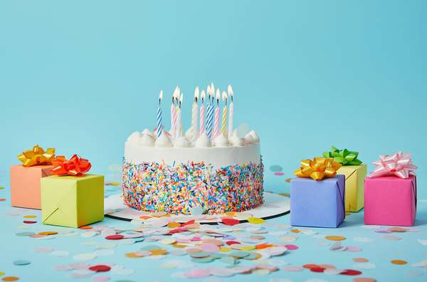 Decorated cake with lighted candles, gifts, and confetti on blue background. (celebrations, cakes, pastry, birthday, anniversary)