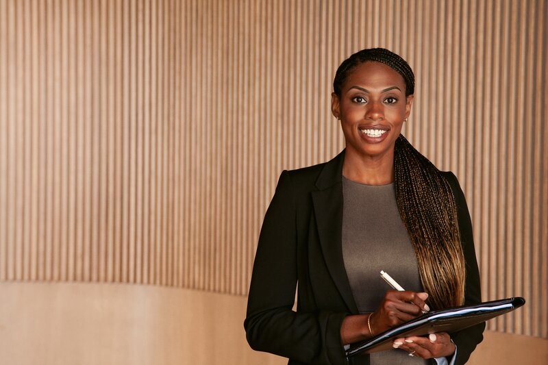 A woman wearing a black business suit writes on a pad of paper.