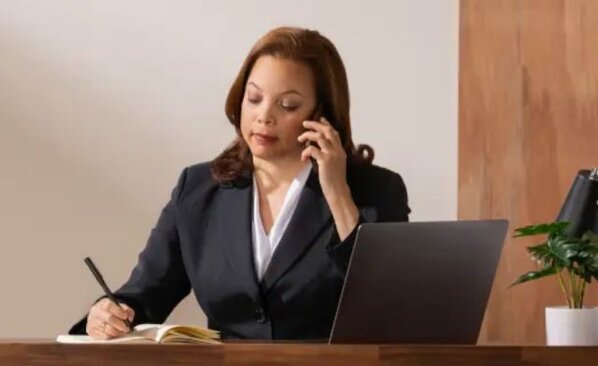 woman sitting at her desk making a call and taking notes.