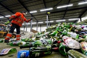 Een medewerker van een glasrecyclingbedrijf verwerkt een enorme hoeveelheid flessen.