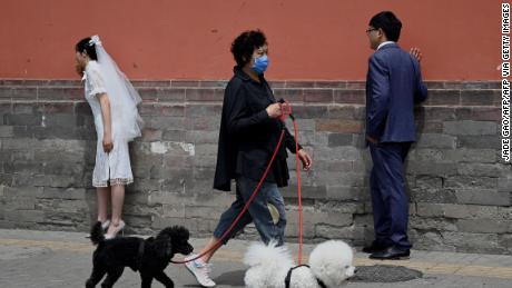 A woman walks her dogs past a couple posing for wedding photographs in Beijing on May 16, 2021. (Photo by Jade Gao / AFP) (Photo by JADE GAO/AFP via Getty Images)