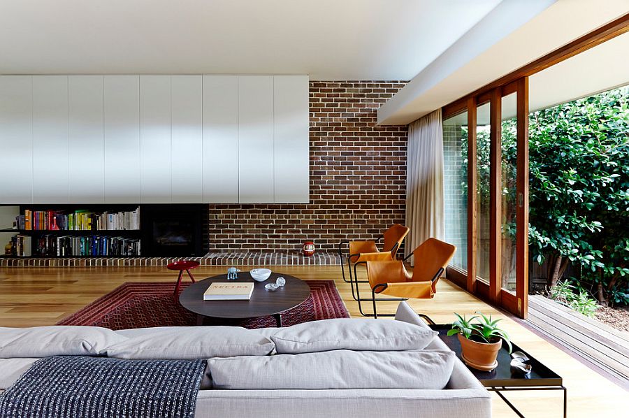 Modern living room mixes brick wall with contemporary shelves in white [Design: Downie North Architects]