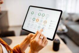 A woman holding up a tablet with a number of smart home controls up on the screen.