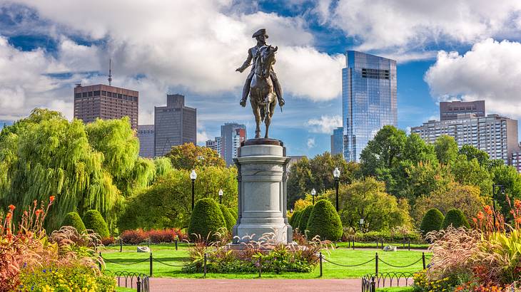 Monument in the center of a park surrounded by trees, with skyscrapers behind