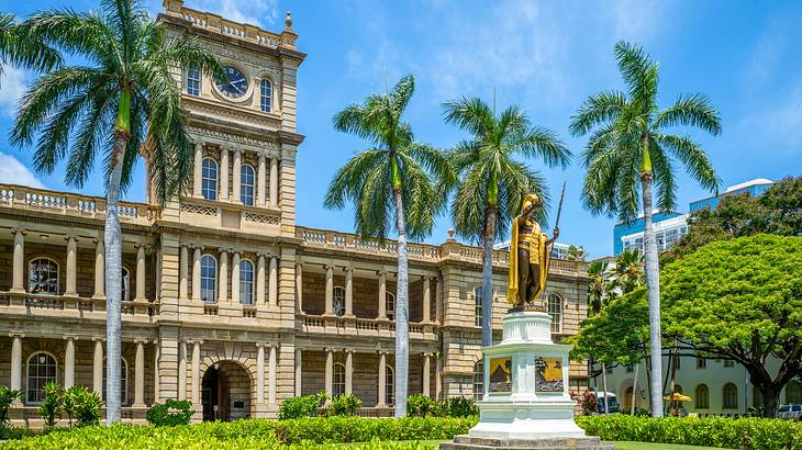 A palace surrounded by a well-kept garden facing palm trees on a sunny day