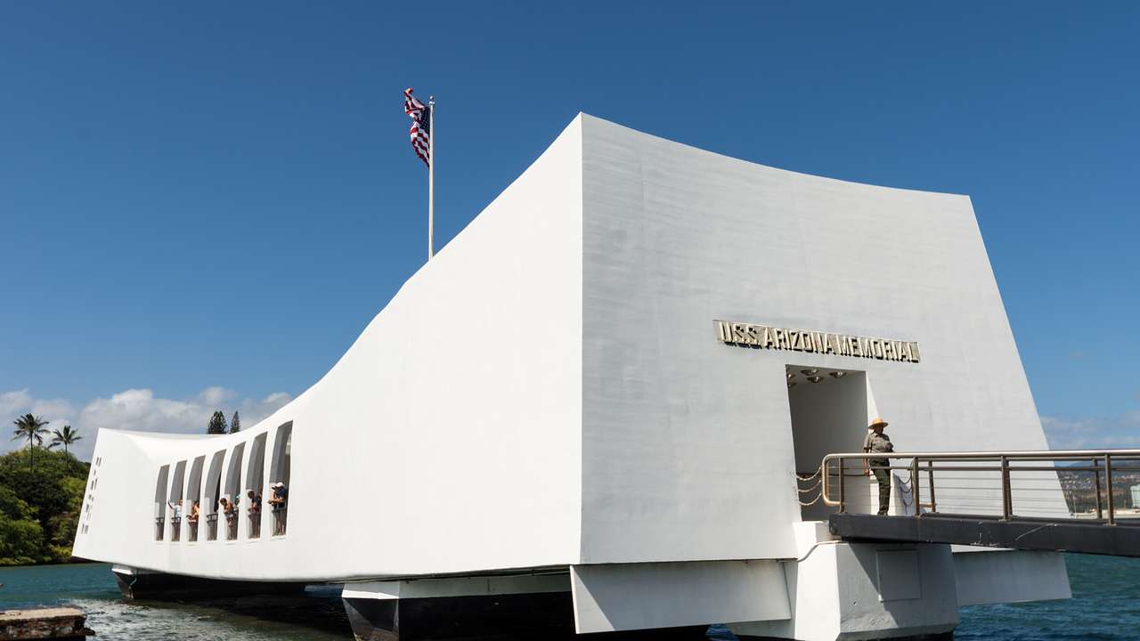 A low white concrete memorial on the water with greenery behind from a distance