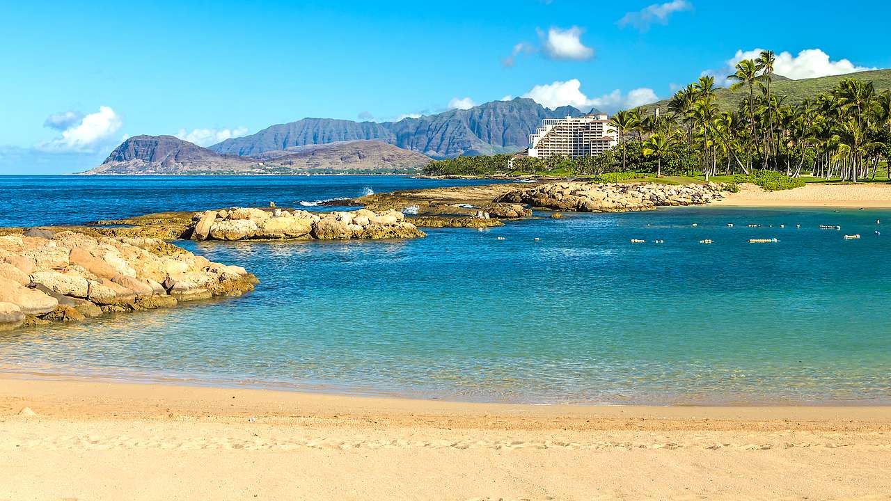 Stunning sandy beach with rocky formation connecting to an opposite shore with trees