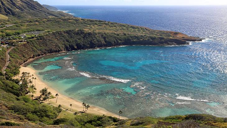 View of a white sand beach in a bay with blue water surrounded by cliffs and greenery