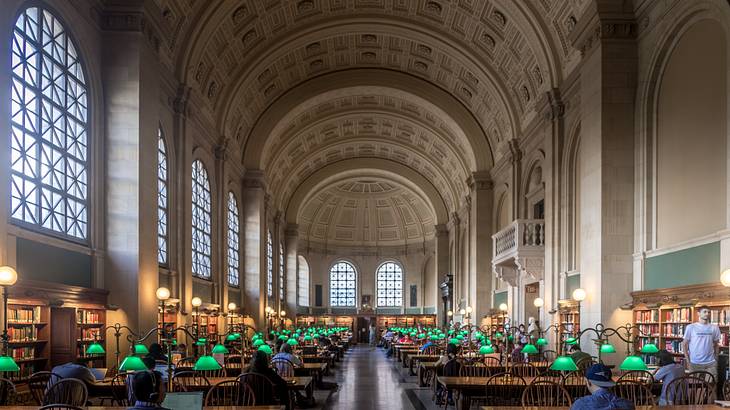 People seated in a high-arched library hall with desks and lighted lamps