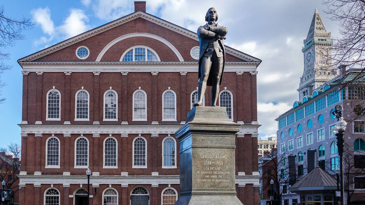 A red-bricked building facing a statue under a partly cloudy sky