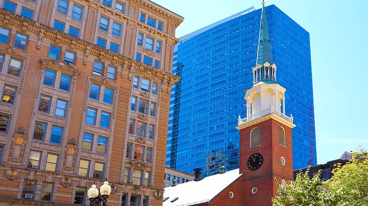 A pointy church top with a tree on the right and surrounded by buildings