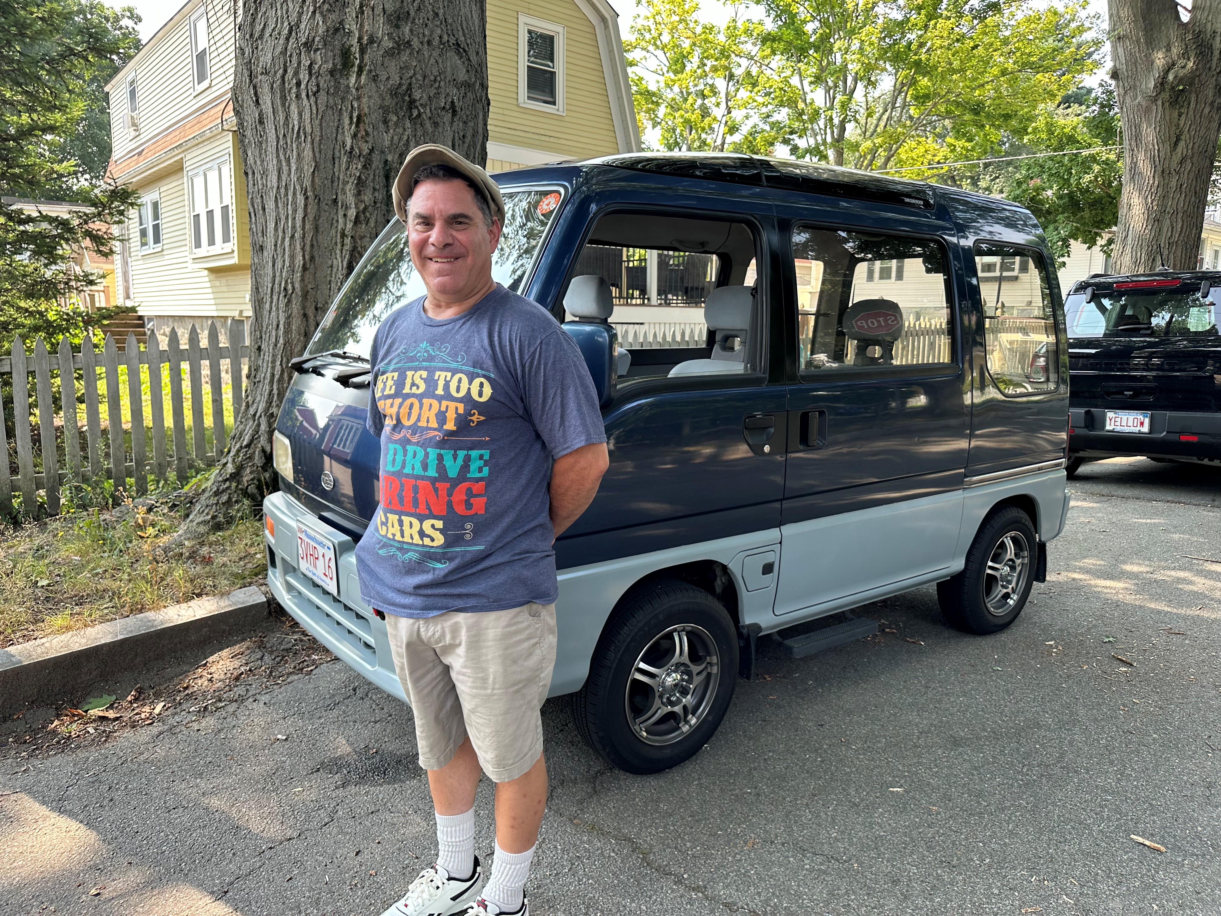 A man stands next to a van that is slightly shorter than he is.