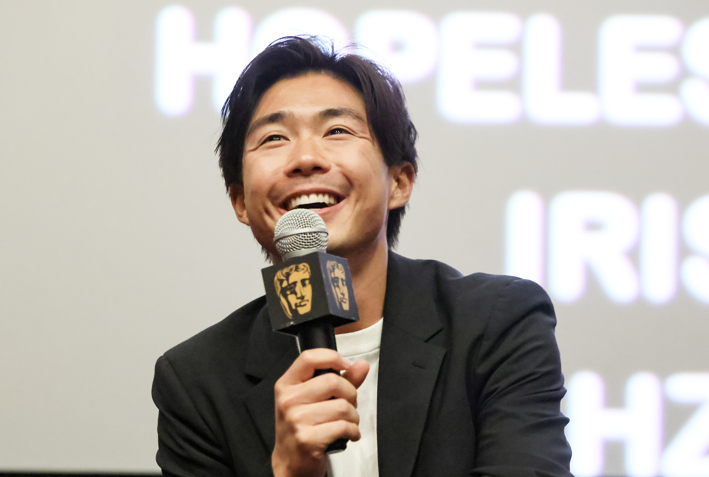 A man smiles and laughs as he holds a microphone on stage at a film screening.