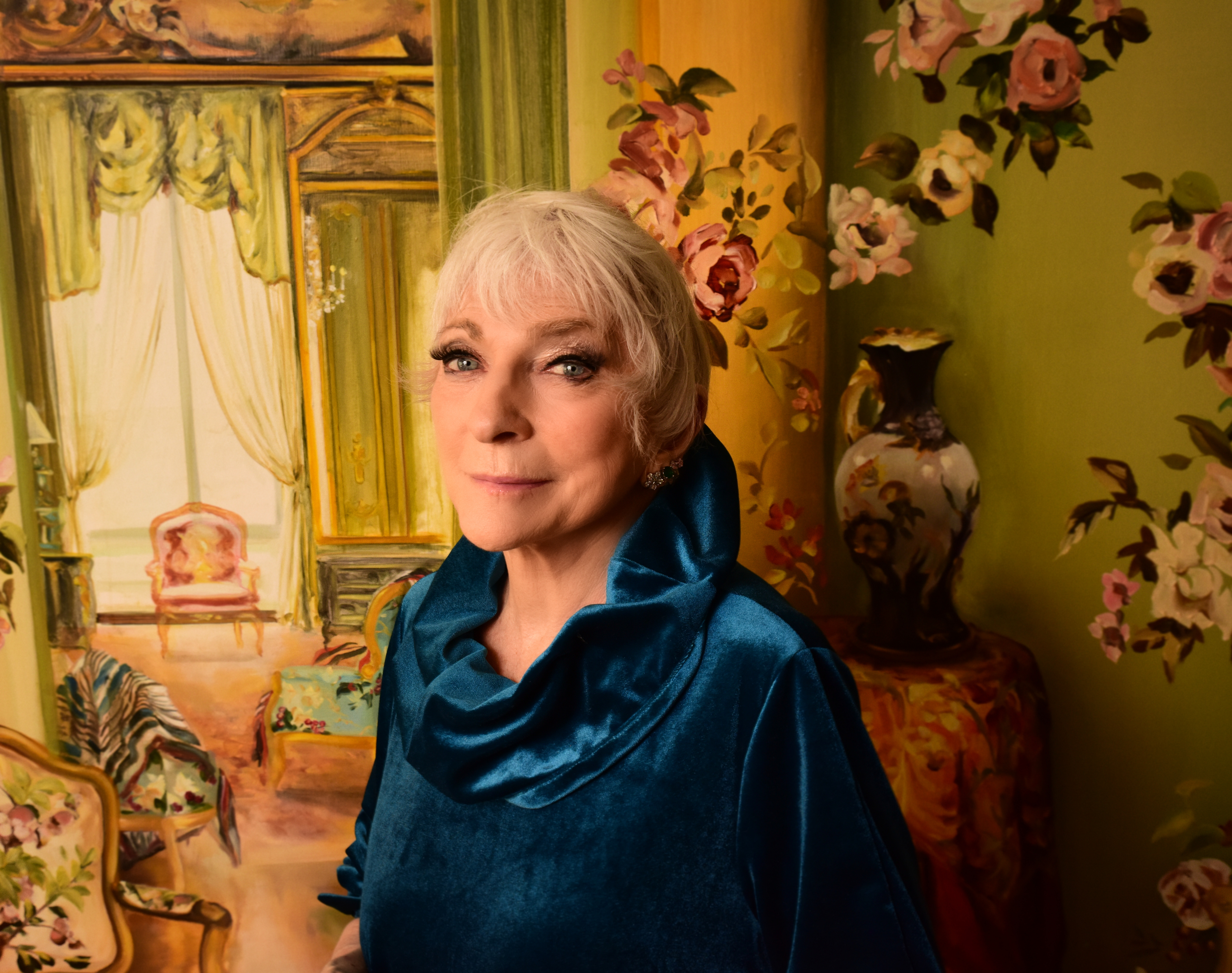 Judy Collins, in a blue shirt, looks at the camera in a green room.