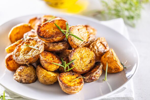 Golden baked potatoes on a white plate with rosemary.