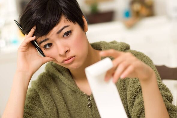 Young woman with distressed expression holding invoice