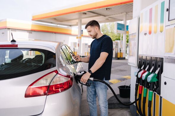 Bearded man refuelling car on gas station and looking into his smartphone. Man compares fuel prices