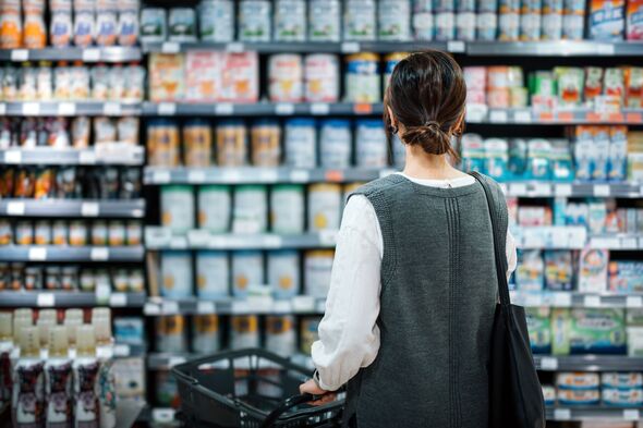 Rear view of young Asian mother with a shopping cart grocery shopping for baby products in a supermarket. She is standing in front of the baby product