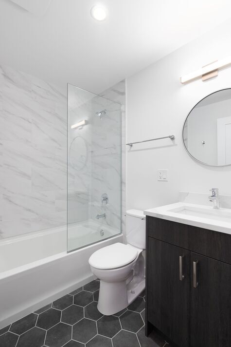 A bathroom with wood cabinet, hexagon tile floor, and marble shower.