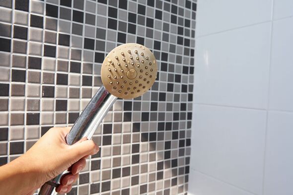 Woman holding in hand corroded limescale calcified old shower head hanging from a stand inside cabin