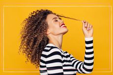 Woman with curly hair side view with her pulling at one of the curls