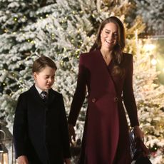 Prince William wears a black coat and Kate Middleton wears a dark red coat as they hold hands with their children Princess Charlotte and Prince George while walking in the snow