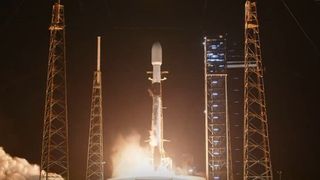 a white rocket launches at night above a vright plume of fire