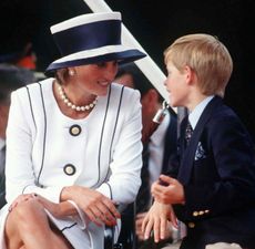 Princess Diana wearing a white suit and hat talking to a young Prince Harry