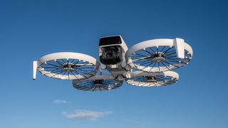 The DJI Flip drone, in white with four propellers is mid flight with clear blue skies behind it and one small grey cloud just below it.