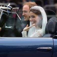 Kate Middleton wearing a veil and tiara with her wedding dress riding in a blue convertible next to Prince William after their wedding