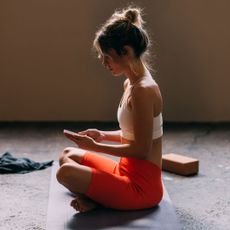 A woman on her phone in gym wear prior to doing some of the best Pilates exercises