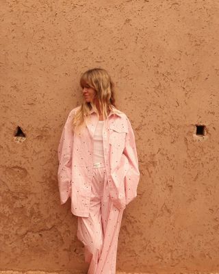 Woman standing against a wall with striped pink shirt and matching pants