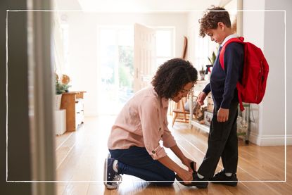 Mother helping child try on his school uniform, including school shoes, in the hallway at home