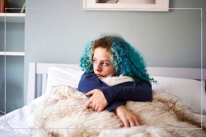 A teenage girl looking sad while sat up in bed