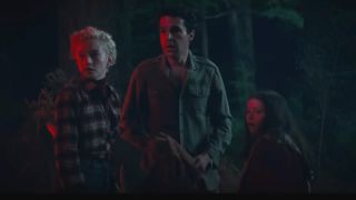 Julia Garner, Christopher Abbott, and Matilda Firth stand stunned in the dark woods bathed in red light in Wolf Man.