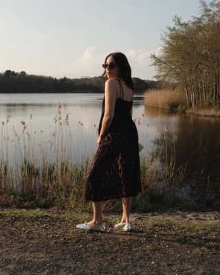 Woman standing in front of a lake with a see-through lace skirt, black tank, and silver flats