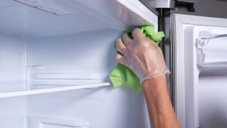 Gloved hand cleaning a fridge interior