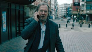 Gary Oldman walks down the street on the phone in Slow Horses