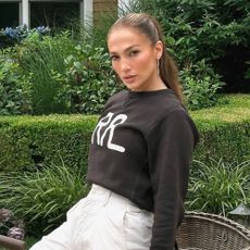 Jennifer Lopez wears cropped trousers, white sneakers, and a black sweater while sitting on a bike.