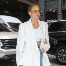 jennifer lopez wears a white blazer and bra top with orange sunglasses and jeans