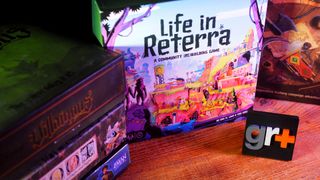 A stack of board games on a wooden table beside Life in Reterra and Gloomhaven: Jaws of the Lion, all behind a GamesRadar+ logo