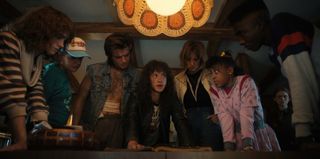 Most of the kids huddled around a table in a press image for Stranger Things 4