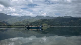 People on a small wooden boat gliding across Lake Kivu with hills in the background.