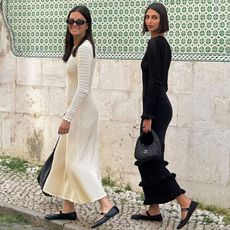 French influencer Salome Mory and her mother walking on a sidewalk in Lisbon, Portugal in black and beige knitted long-sleeve maxi dresses with black bags and black Mary Jane ballet flats