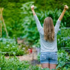 Gardener stretches out in garden holding hand trowel