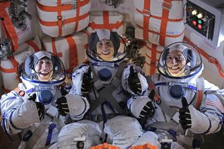 Three people in astronaut suits smile for a photograph and all are giving a thumbs up gesture.