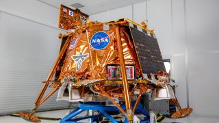 a cube-shaped spacecraft covered in gold foil sits on a dolly in a white cleanroom 